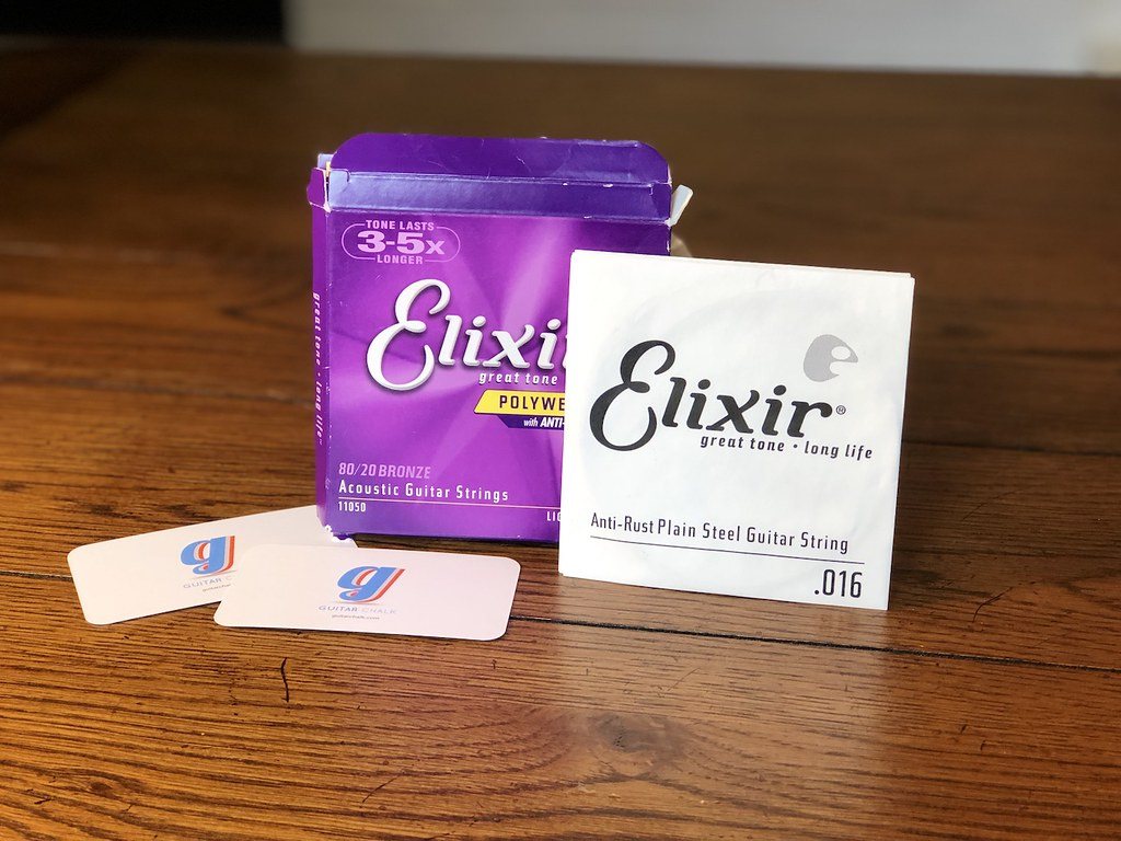 Image de guitare acoustique Boîte et pochette de cordes de guitare Elixir sur table en bois