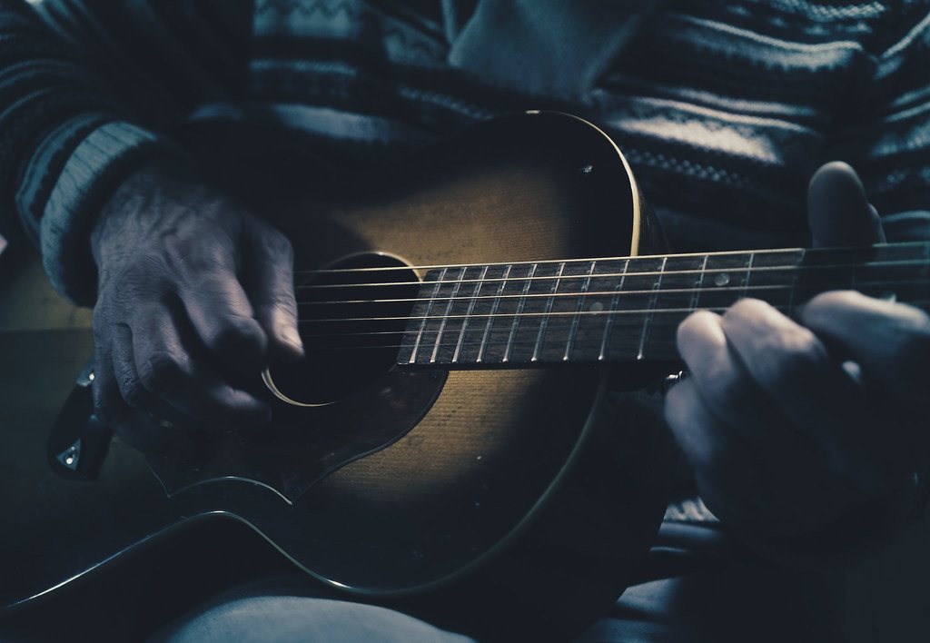 Image de guitare acoustique Mains jouant une guitare acoustique sombre dans une lumière bleutée