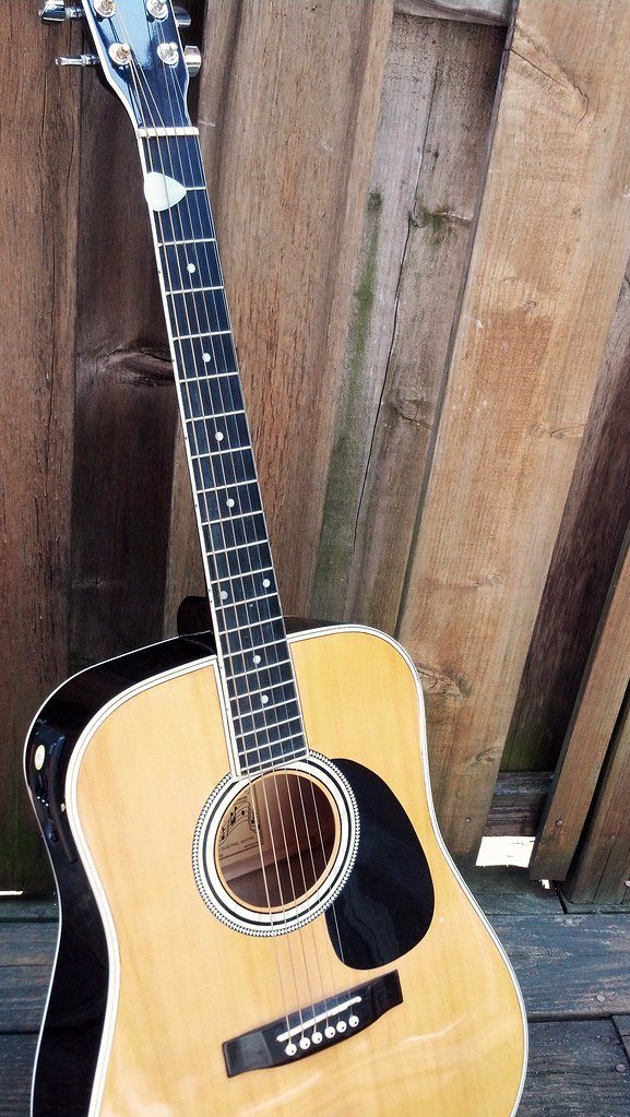 Acoustic guitar image acoustic guitar light-colored leaning against a fence wooden